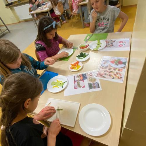 Kinder um einen Tisch schneiden Gemüse