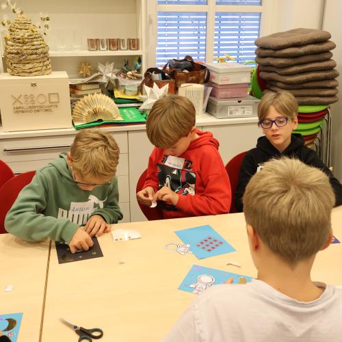 Kinder sitzen an Tisch und basteln