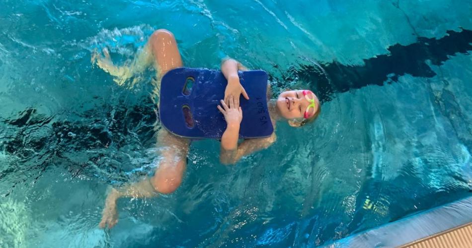 Kind mit Schwimmbrett beim Rückenschwimmen